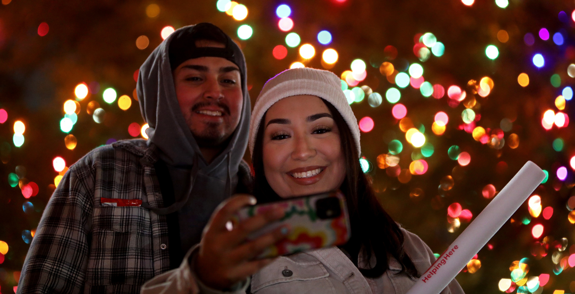 Man and woman smile while taking a selfie underneath the lights