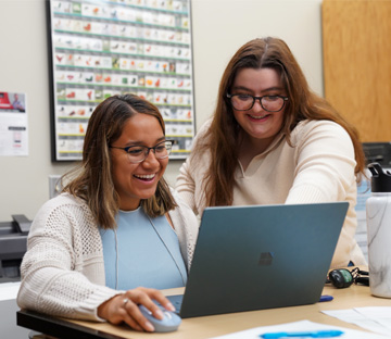 A student on their computer helped by their teacher