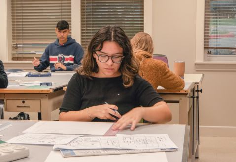 Student sitting at a work table drafting architectural drawings