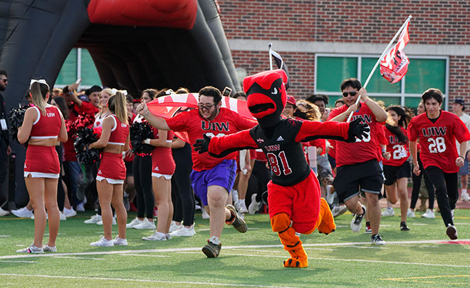 Red the Cardinal and students running across football field 