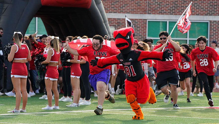 Red the Cardinal and students running across football field