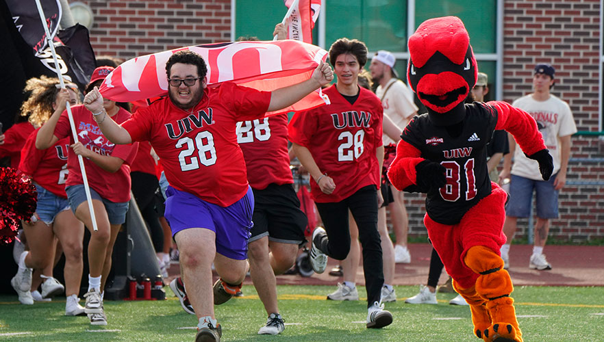 Red the Cardinal and students running across football field