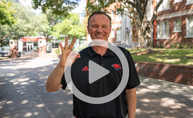 President Evans showing Cardinal hand sign with video play button 